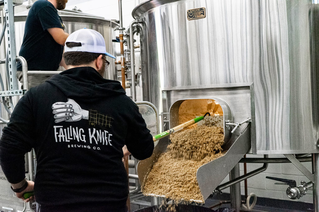 Falling Knife Brewing Co. brewer shoveling grains